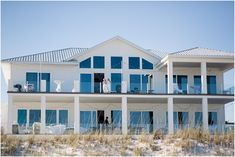 a large white house with blue windows on the beach