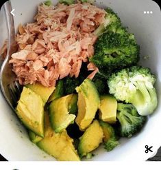 a white bowl filled with broccoli and other vegetables next to a fork in it