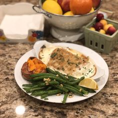 a white plate topped with green beans and potatoes next to a bowl of oranges