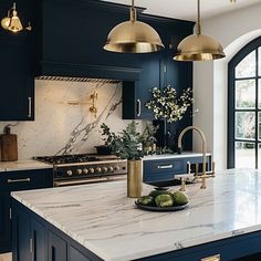 a kitchen with marble counter tops and gold pendant lights hanging over the stove top island