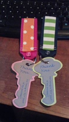 two key shaped tags sitting on top of a wooden desk next to a computer keyboard