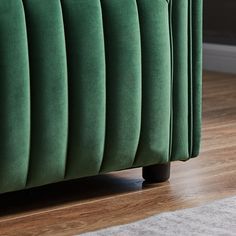 a green velvet bed with wooden legs and headboard on hardwood flooring in living room