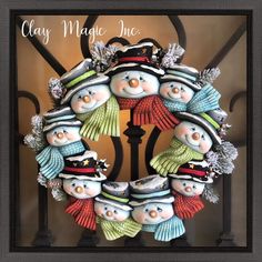 a christmas wreath with snowmen and hats hanging on a wrought iron gate that reads clay magic inc