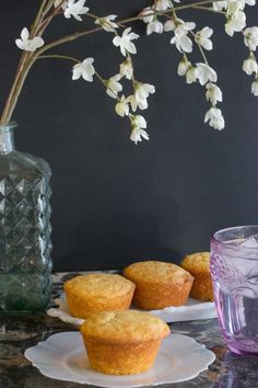 some muffins are sitting on plates next to a vase with flowers in it