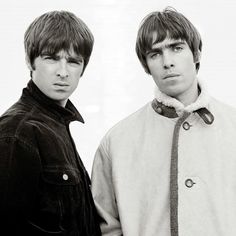 two young men standing next to each other in front of a white wall and wearing jackets