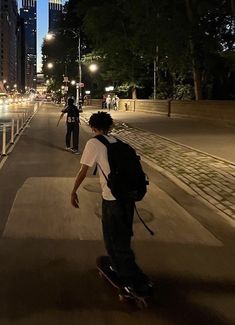 two skateboarders are riding down the sidewalk in the city at night with their backpacks on