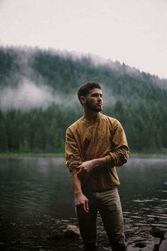 a man standing in front of a body of water with mountains in the back ground