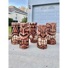 four wooden tiki statues sitting in front of a garage