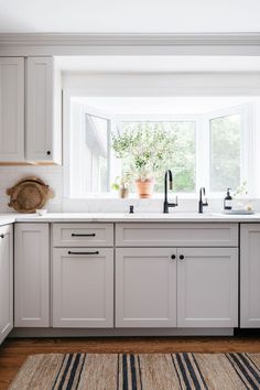 View of kitchen renovation. Sink area with bay window. White cabinets with black cabinet and drawer pulls, white ceiling, hardwood floors with striped jute rug. White countertops. Kitchen Design With Window, Kitchen Bay Window Over Sink, Kitchen Windows Above Sink Ideas, Kitchen Windows Above Sink, Window Above Kitchen Sink, Traditional Kitchen Renovation, Sink Window, Window Over Sink