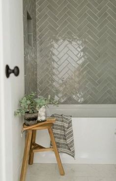 a white bath tub sitting under a window next to a wooden stool and potted plant