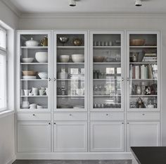 a kitchen with white cabinets and black counter tops in front of a large glass doored cabinet