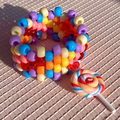 Kandi bracelet with colorful beads and matching lollipop charm. Bracelet has a base of 28 beads.  Bead Colors: Yellow, white, blue, red, purple, orange, pink, lollipop charm Measurements: 17.5 - 23 cm l, 3.5 cm w The length measurement is of the circumference of the bracelet. The first number is the inner circumference, the second is the outer circumference. All bracelets are stretchy and size my vary slightly due to the elastic stretch. When putting on and taking off your cuff bracelet make sure to slide/push wiggle the bracelet onto your hand, as opposed to pulling and stretching the bracelet onto your wrist. Too much stretching and pulling can rip and break the elastic. Handmade Sweet Style Multicolor Beaded Bracelets, Sweet Multicolor Beaded Bracelets, Sweet Multicolor Round Bead Bracelets, Pony Bead Jewelry, Bracelets Kandi, Pony Bead Animals, Pink Lollipop, Pony Bead Bracelets, Pony Bead Crafts