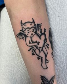 a black and white tattoo on the arm of a person with a devil head holding a heart