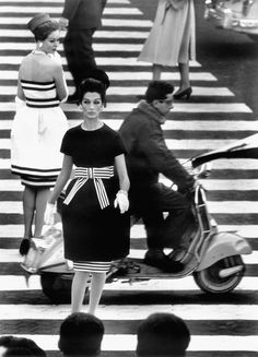 black and white photograph of people walking across a crosswalk with scooter in the foreground