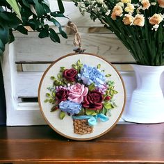 a basket with flowers in it sitting on a wooden table next to a vase filled with flowers