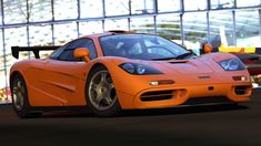 an orange sports car driving on a race track in front of a large glass building