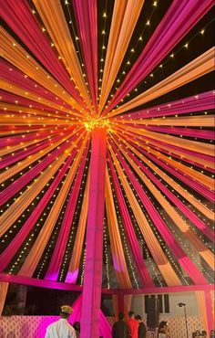 the inside of a tent decorated with pink and orange ribbons, lights and draping