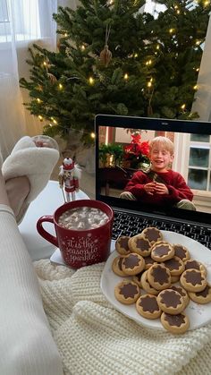 a laptop computer sitting on top of a desk next to a plate of cookies and cup of coffee