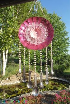 a pink flower with spoons hanging from it's side in front of some trees