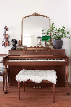 an old piano is sitting in front of a mirror and bench with a plant on it