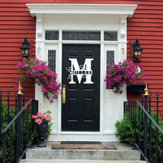 a black door with the letter m on it and some flowers in front of it