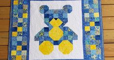 a blue and yellow quilt with a teddy bear on it's back, sitting on a wooden floor