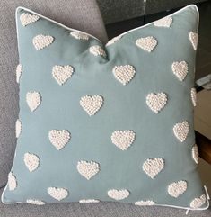 a blue pillow with white hearts on it sitting on a gray couch next to a chair