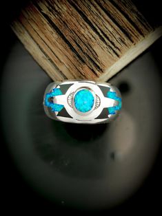 a silver ring with blue opal inlays sits on top of a piece of wood