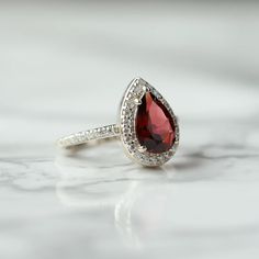 Looking for a ring that just demands attention? The Britney ring will definitely draw eyes, with a spectacular design and colorful Garnet as the main stone, bedazzled with moissanite. A truly unique ring to treat yourself to. Details: Center stone Gemstone: Garnet Stone Shape: Pear Measurements: approx. 10x7mm Side stones Gemstone: Moissanite Shape: Round Measurements: 1.3mm (37) Band measurements: approx. 1.8mm wide, approx. 1.5mm thick Pictured in vermeil, available also in sterling silver or Lab-created Ruby Ring With Accent Stones As Gift, Dazzling Gemstone Rings For Proposal, Heirloom Pear-shaped Diamond Ring With Gemstone, Teardrop Diamond Jewelry For Proposal, Cubic Zirconia Jewelry With Accent Stones For Proposal, Moissanite Teardrop Diamond Ring With Center Stone, Teardrop Moissanite Diamond Ring With Center Stone, Silver Halo Teardrop Rings, Cubic Zirconia Ring With Accent Stones For Proposal