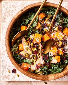 a wooden bowl filled with salad and two gold serving spoons on top of it