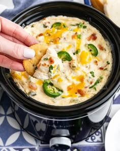 a hand dipping a piece of bread into a bowl filled with cheesy dip