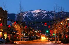 a city street with christmas lights on the trees and mountains in the background at night