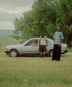 two people standing next to a car in a field