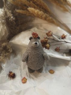 a crocheted teddy bear with a flower on its head sitting next to dried flowers