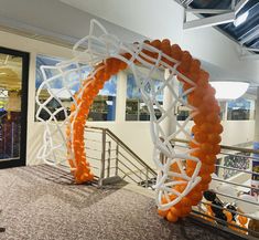 an orange and white balloon arch in the middle of a room with stairs leading up to it