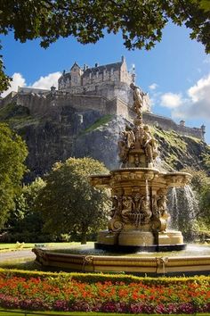 a fountain in the middle of a garden with a castle in the background