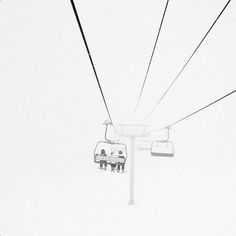 two people sitting on a ski lift in the snow with one person standing at the bottom