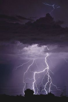 lightning strikes in the night sky over power lines and telephone poles on a cloudy day