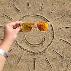 someone is holding their sunglasses in front of the sun drawing on the sand with them