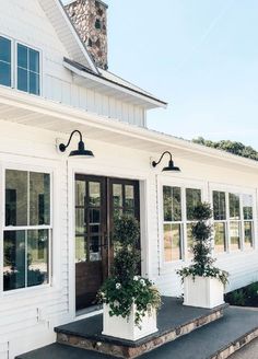 a white house with two large potted plants on the front porch and windows above it