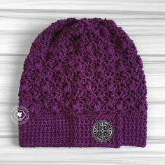 a purple crocheted beanie with a button on the front and an embellishment in the middle