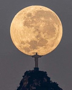 the full moon is seen behind a statue on top of a hill