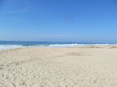 an empty beach with waves coming in to the shore and blue sky above it, on a sunny day