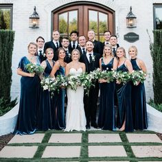 a group of people standing in front of a building with flowers and greenery around them