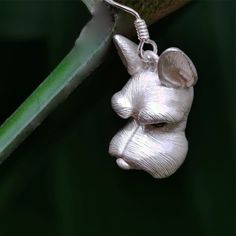 a silver dog charm hanging from a green leaf