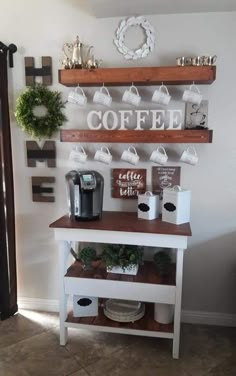 a coffee bar with cups and mugs on the shelves above it is decorated with greenery