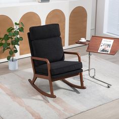 a black rocking chair sitting on top of a white rug next to a potted plant