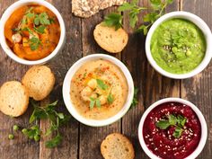 four bowls of soup and crackers on a wooden table with green garnish