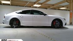 a white car parked in a garage with red rims on the tires and wheels