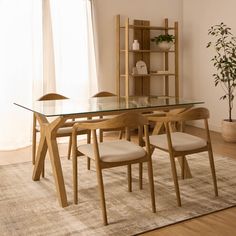 a glass table with four chairs in front of a book shelf and potted plant